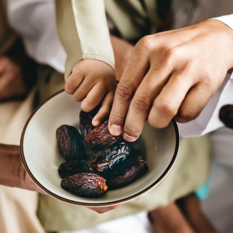 close up to hands reaching for a bowl of dates
